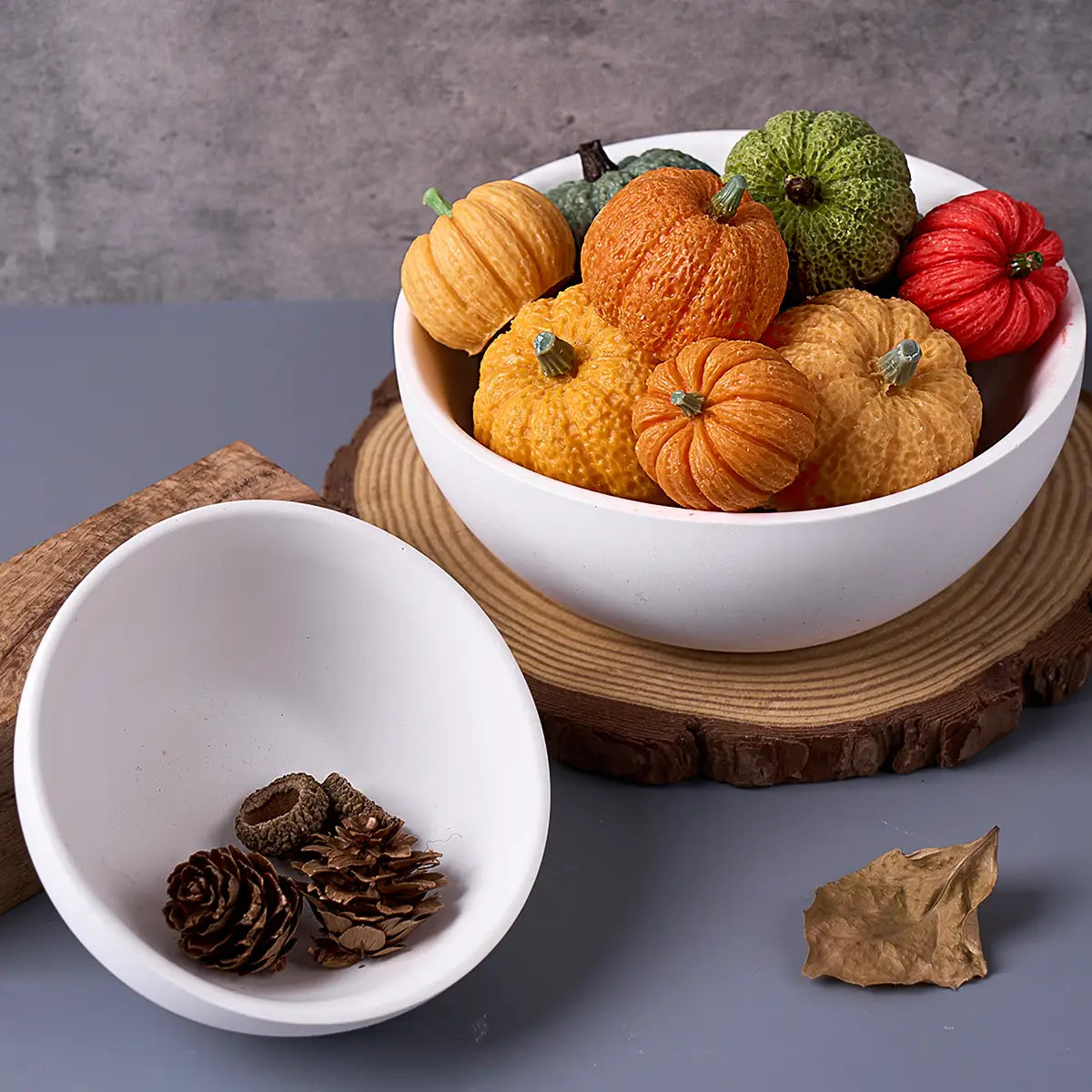 A round white ceramic bowl made using a silicone mold for concrete storage bowls filled with miniature decorative pumpkins in orange green and red hues.