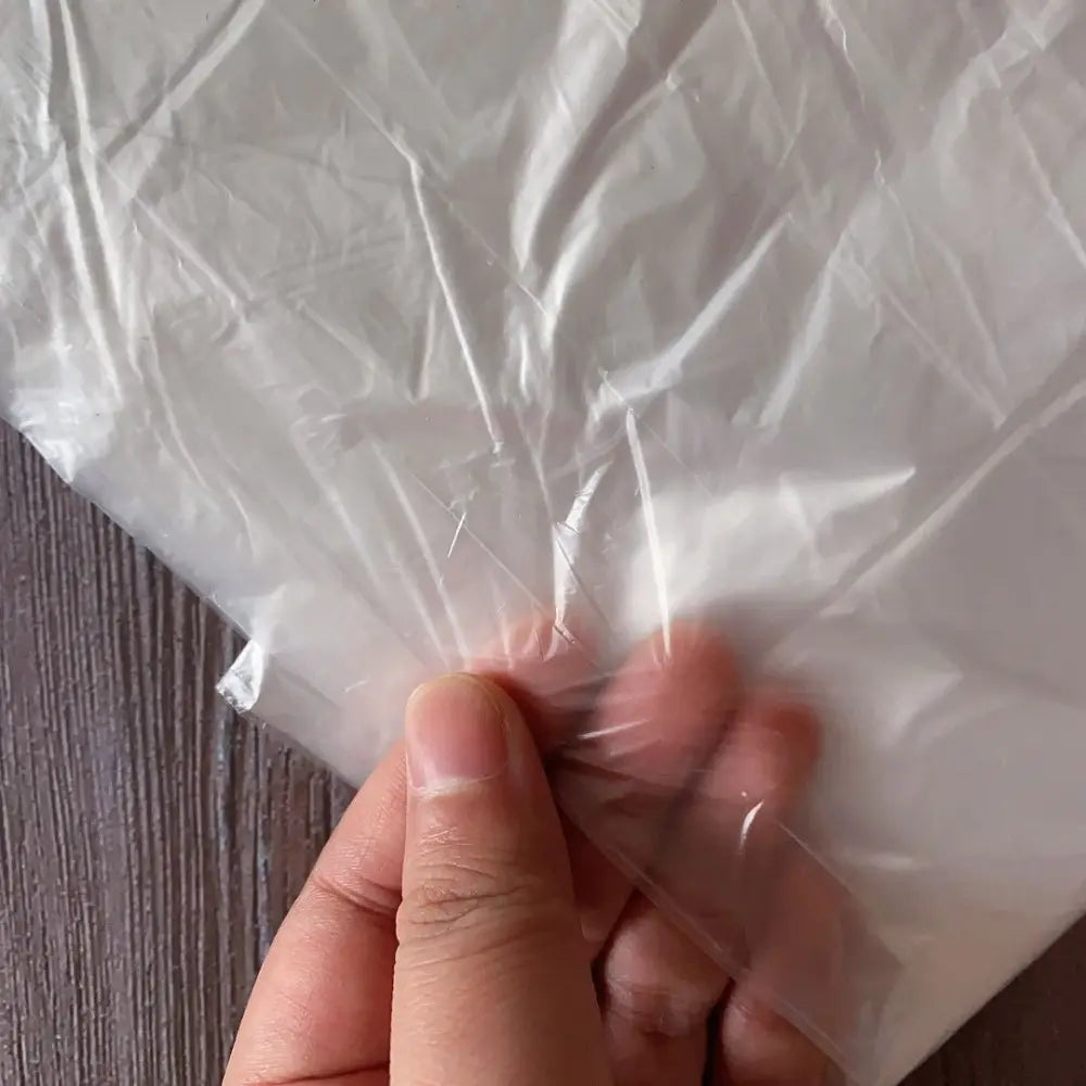 Eine Hand, die einen transparenten Kunststoffbeutel mit einer transparenten Kunststoff-Möbel-Staubabdeckung als Schutzhülle hält.