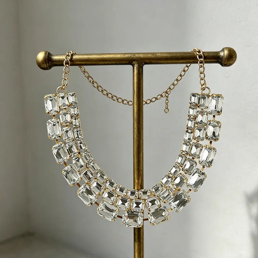 A sparkling gold-toned crystal statement choker necklace for women featuring multiple rows of clear rectangular-cut crystals in a bold design.