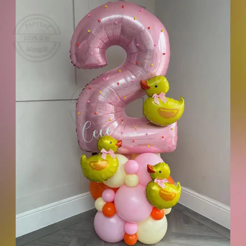 Un globo en forma de número dos rosa hecho de papel metalizado, decorado con figuritas de patitos amarillos y confites de colores para una celebración de cumpleaños.