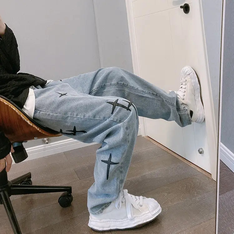 Pantalon cargo en jean à jambes larges à effet délavé clair avec broderie croisée noire, sur les cuisses et les genoux.
