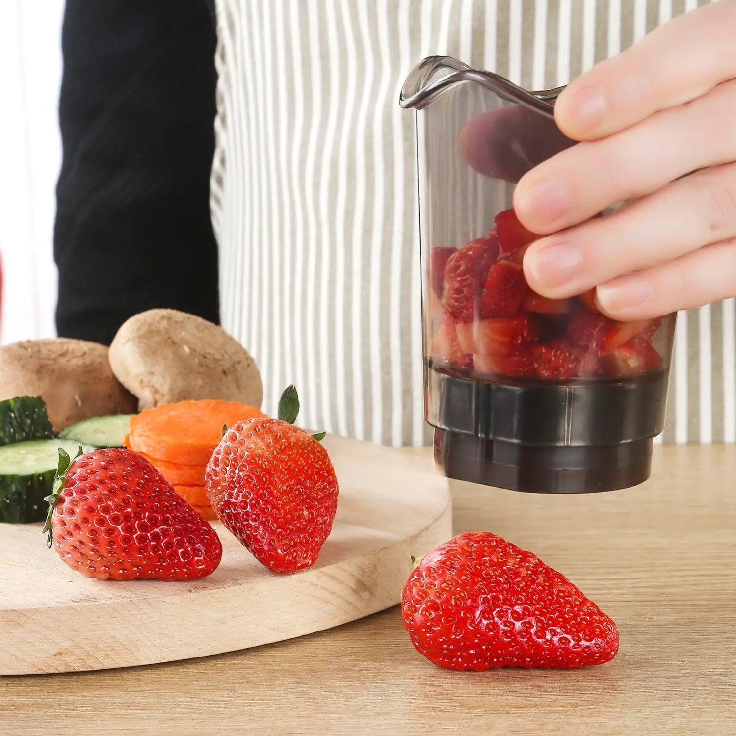 Transparent plastic handheld fruit and vegetable chopper slicer with a black base holding chopped strawberries.