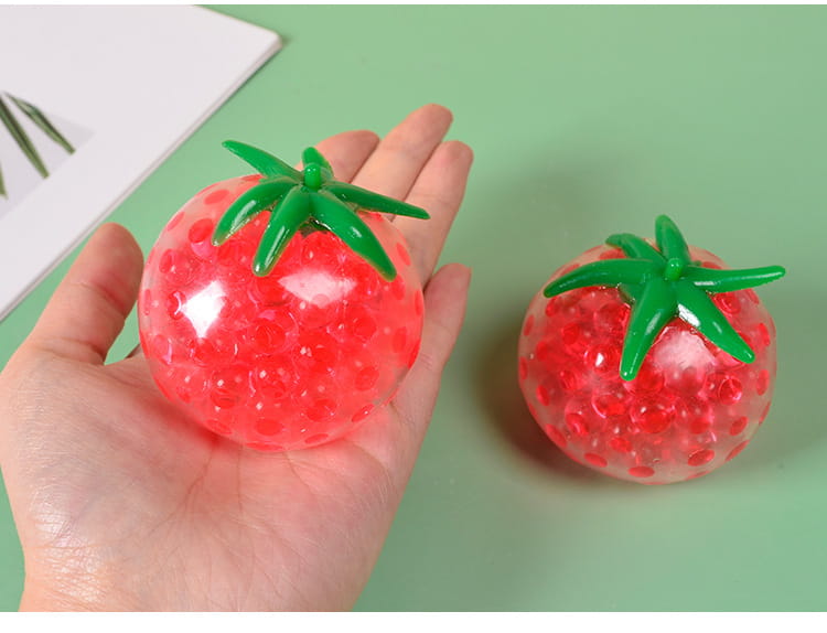 Red tomato-shaped squishy stress relief toy featuring a green plastic stem and translucent gel beads inside for squeezing and stress reduction.