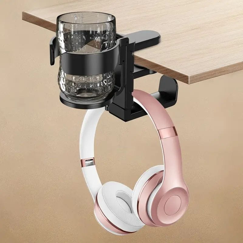 Black desk-mounted cup holder and headphone hook organizer holding a textured glass cup and pink and white over-ear headphones.