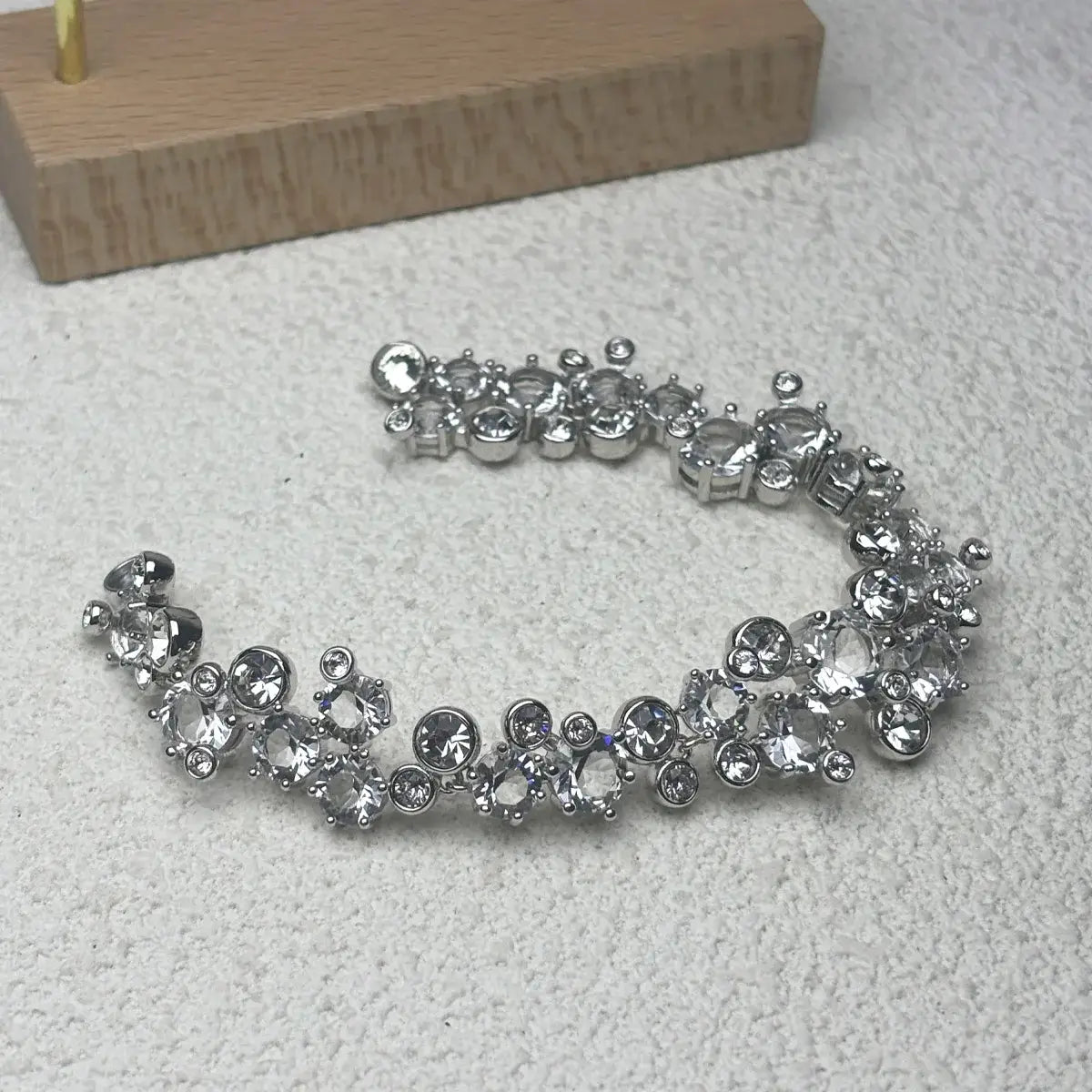 Una pulsera de pedrería plateada con destellos y diseño de racimo, con piedras facetadas transparentes engastadas en eslabones metálicos, de un conjunto de joyería de cristal que incluye un collar de plata y pendientes.