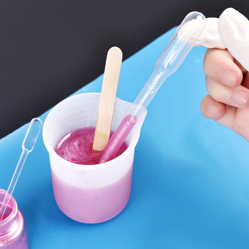 clear plastic pipette with a white bulbous tip transferring pink liquid from a measuring cup in an epoxy resin mixing tool set for diy jewelry making