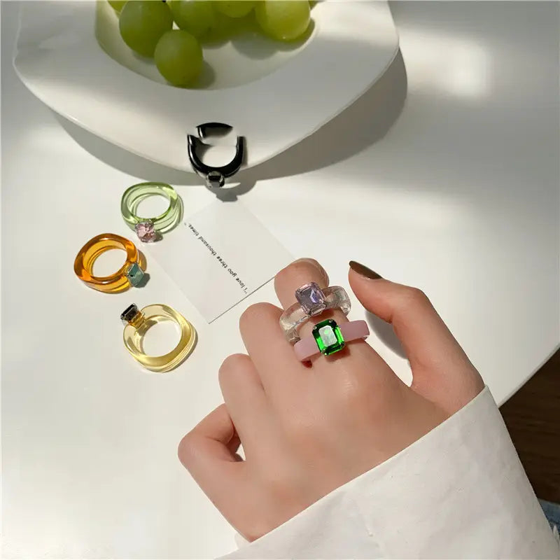 A hand wearing a stack of colorful translucent resin crystal geometric rings with embedded gemstones for women.