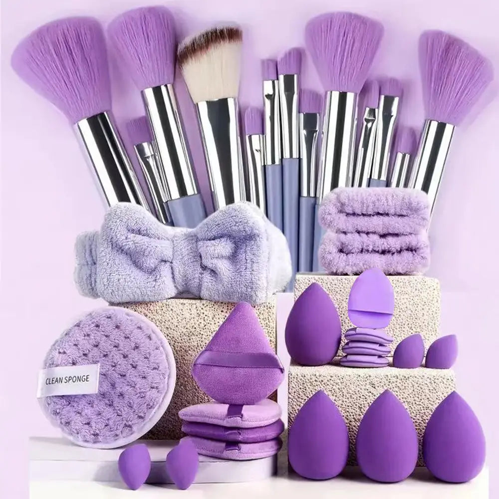 Un ensemble de 33 pièces de pinceaux et d’éponges de maquillage comprenant des pinceaux en nylon pourpre avec des manches argentés et gris, des éponges beauté lavande et un bandeau duveteux assorti.