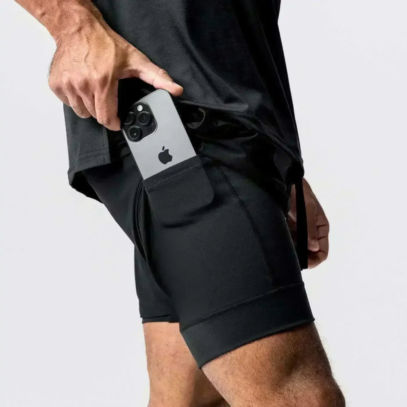 Pantalones cortos de entrenamiento para anime negros 2 en 1 para gimnasio de hombres con cintura elástica y trabilla para la toalla, que presentan un bolsillo lateral integrado que sujeta un iPhone plateado.