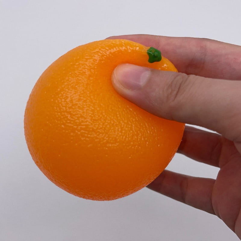 Un anti-stress en silicone texturé orange vif, doté d’un petit détail de tige verte, utilisé comme jouet sensoriel d’anti-stress.