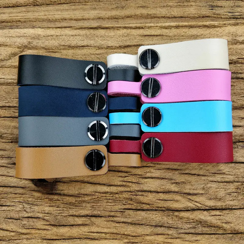 A collection of genuine leather car keychain and metal key ring sets in black navy blue gray tan white pink light blue and red featuring colorful leather strap clips with sleek silver-toned screw-style fasteners.