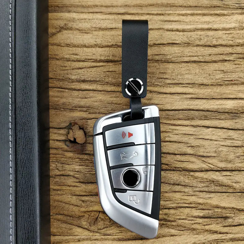 Silver BMW key fob with black accents attached to a genuine leather car keychain and metal key ring set with matching leather strap