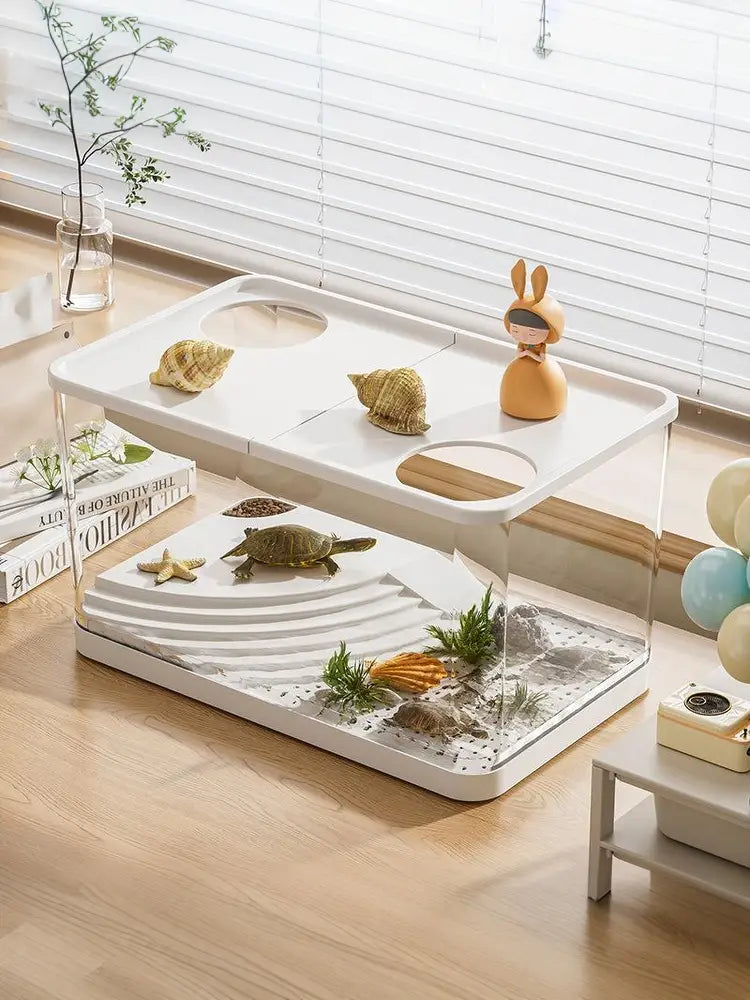 Ökologisches Desktop-Fischbecken mit einem weißen zweistufigen Schildkrötenhabitat mit klaren Acrylseiten, weißem Kunststoffsockel, dekorativen Muscheln, Grünpflanzen, Sand und einer kleinen Schildkröte auf der unteren Ebene.