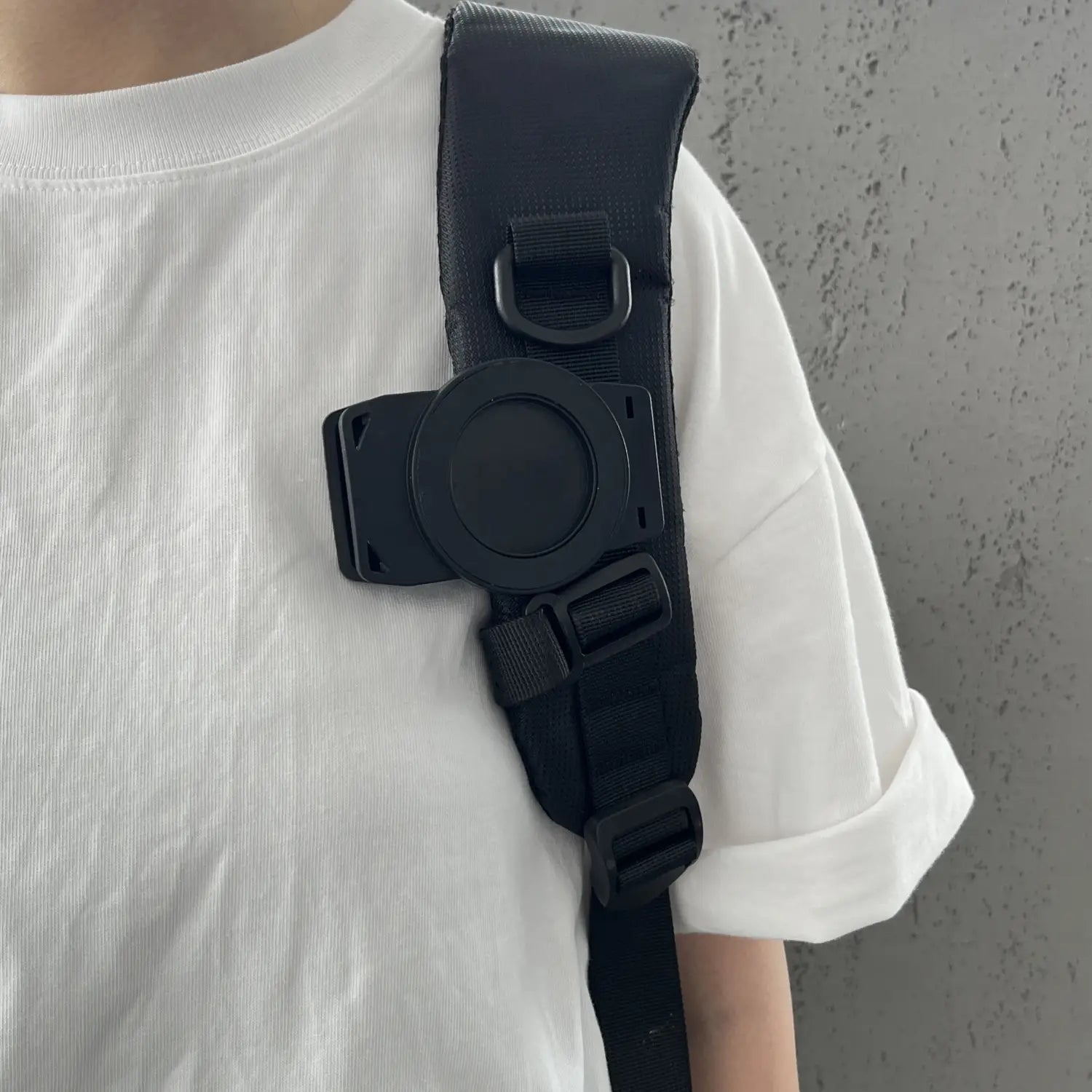 Schwarzer verstellbarer Schulterriemen mit kreisförmiger Kamerahalterung und Schnallensystem für die magnetische Telefon-Rucksackclip Universalhalterung, dargestellt auf der Rückseite des Produkts