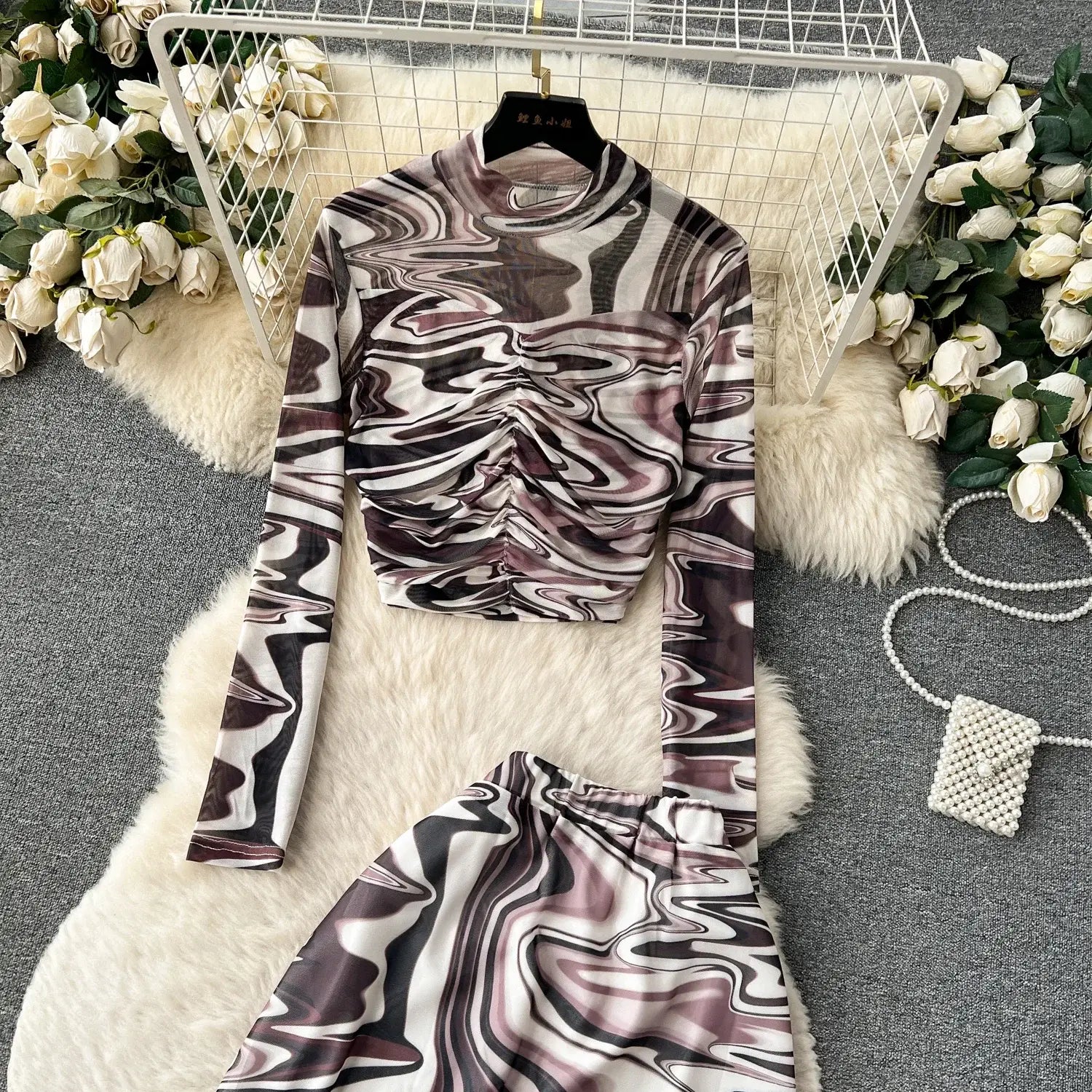 A two piece mesh skirt set features a sheer long sleeved top with a high neckline and ruched waistband in an abstract marbled pattern of white black and muted purple with elastic closure.