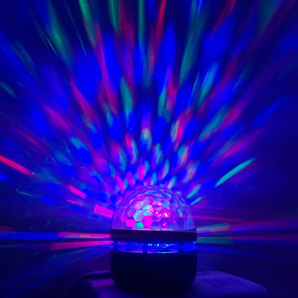 Une veilleuse de projection de ciel étoilé comprenant une coupole transparente facettée lumineuse, émettant des faisceaux bleus et roses vibrants.