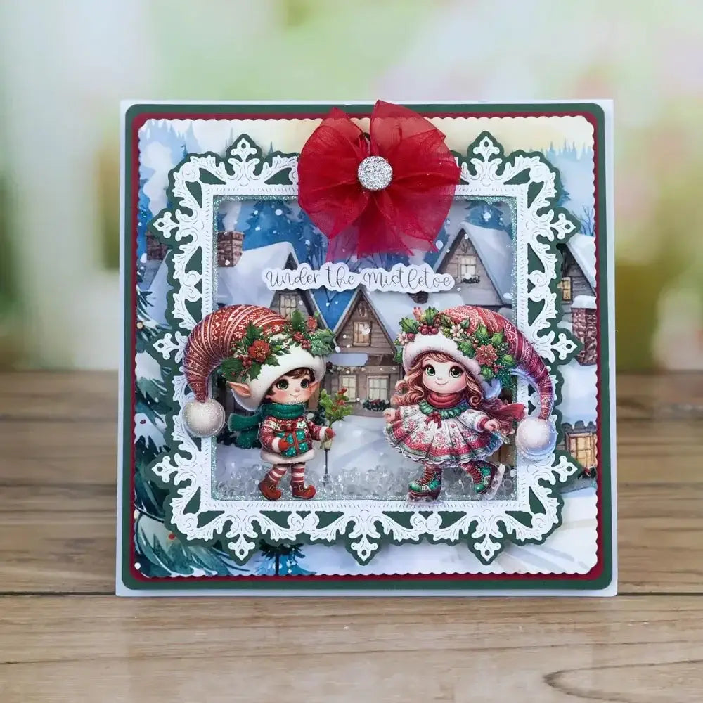 A festive Christmas metal cutting die and stamp set featuring two illustrated elves in red and green holiday attire framed by intricate white lace borders with a large red bow at the top.