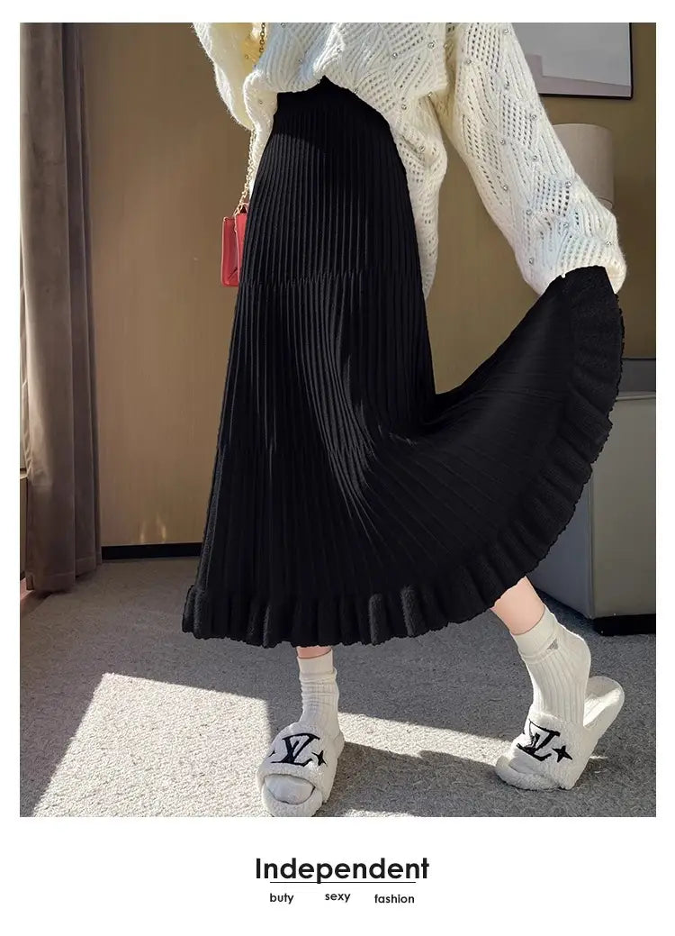 Jupe mi-longue en maille noire, à taille haute, plis et nervures verticales discrètes, avec ourlet évasé dans un style parapluie à plis