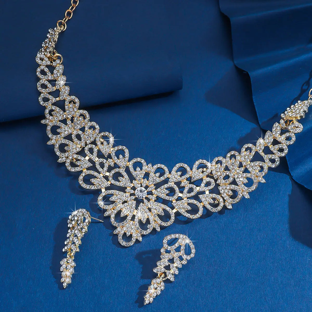 Un ensemble de bijoux en forme de fleur en cristal rose plaqué or, comprenant un collier à la finition ton or au motif floral complexe, agrémenté de cristaux clairs étincelants, accompagné de boucles d’oreilles pendantes assorties.