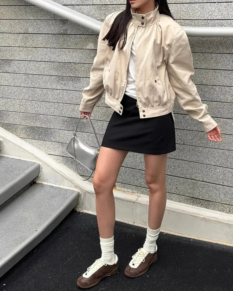 Veste bomber en daim beige à col haut et devant boutonné, associée à des chaussures de tennis blanches légères et respirantes pour un port décontracté.