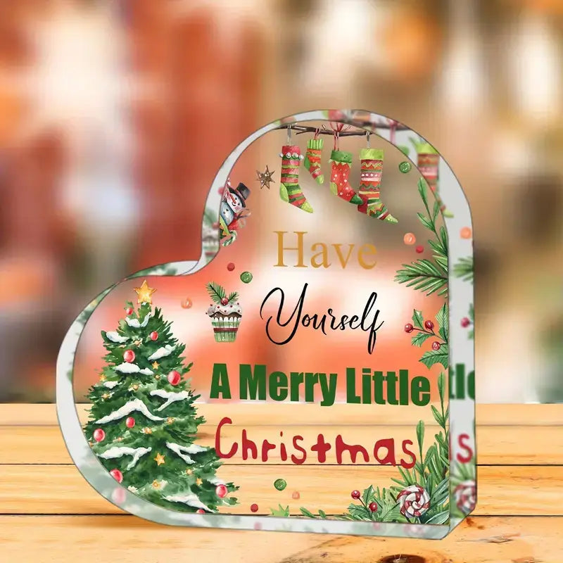 Ein Acryl-Weihnachtsherz-Ornament-Desktopständer mit einer herzförmigen Tafel: ein festlich schneebedeckter Baum, hängende Socken und der Satz „Have yourself a merry little Christmas“ in Gold-, Schwarz-, Grün- und Rot-Schrift.