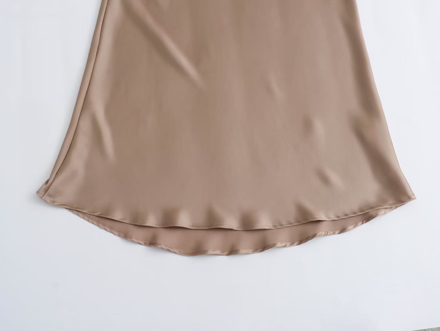 Une jupe midi fluide en satin taupe, à taille haute, finition lisse et brillante et ourlet délicatement froncé.