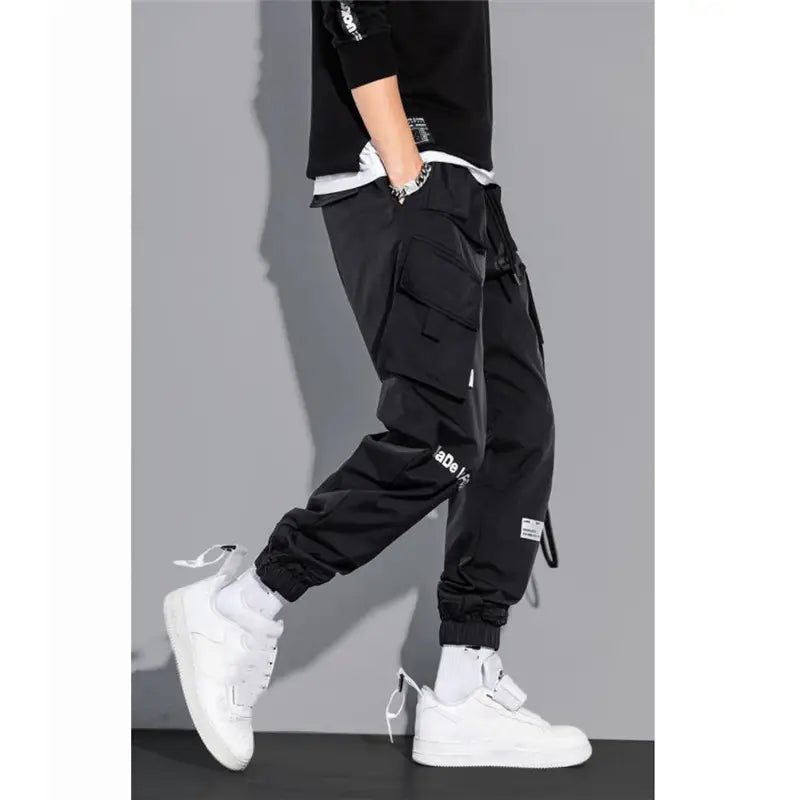 Black mens tactical cargo pants with multiple pockets and white text detailing designed for streetwear.