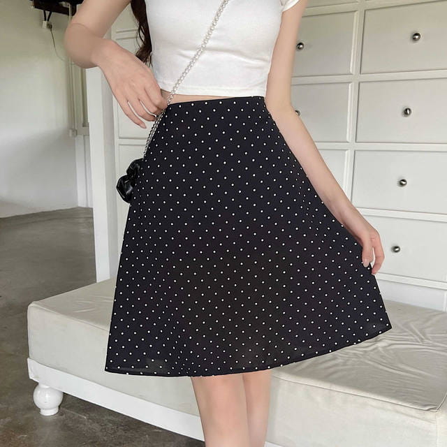 Falda línea A negra con lunares blancos y una pequeña aplicación floral negra en el lateral, en contraste con el título del producto de la falda midi línea A roja con lunares.