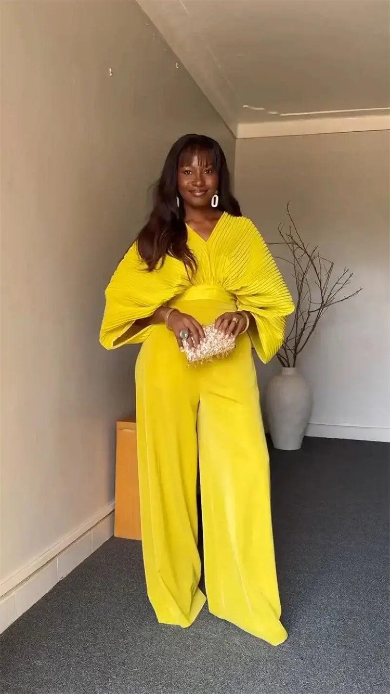 Bright yellow velvet jumpsuit with wide flowing sleeves and a v-neckline featured alongside a purple satin two piece set with wide leg pants.