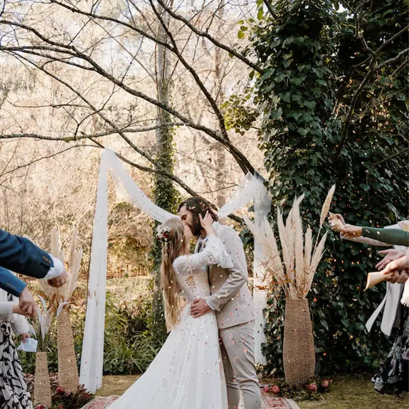 Die Braut trägt ein fließendes weißes Spitzenhochzeitskleid mit zarter Verzierung und langen Ärmeln, zusammen mit personalisierten Hochzeits-Konfetti-Tüten, 30 Stück, für einen festlichen Anlass.