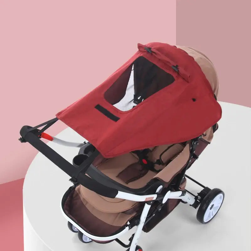 Roter Stoff für den universellen Kinderwagen-Sonnenschutz mit UPF50-Dach und einer klaren Fenster-Panel-Ausführung, ausgelegt, um Sonnenschutz zu bieten.