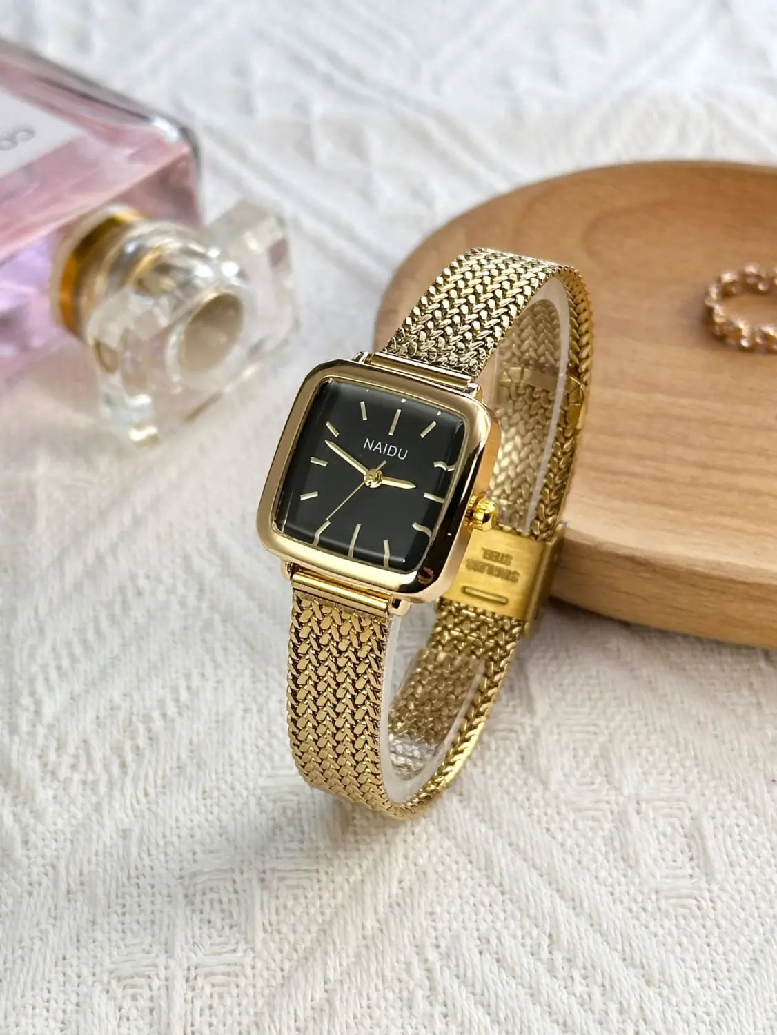 Minimalist square quartz watch for women featuring a gold mesh bracelet and a square black dial with gold hands and the brand name Naidu on the face.