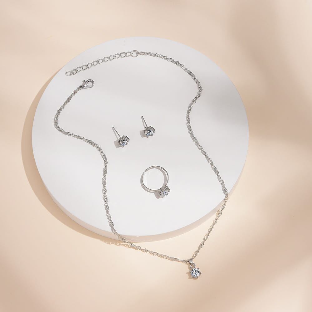 Juego de joyería de 5 piezas con circonitas cúbicas de color plateado, que presenta un collar de cadena delicada con un dije de cristal colgante, aretes tipo botón a juego y un anillo adornado con piedras brillantes transparentes.