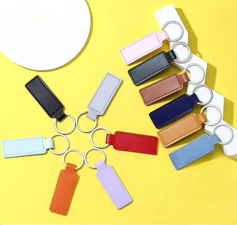 A collection of customized leather keychains featuring rectangular shapes with stitched edges in assorted pastel and bold colors attached to silver-toned metal rings.