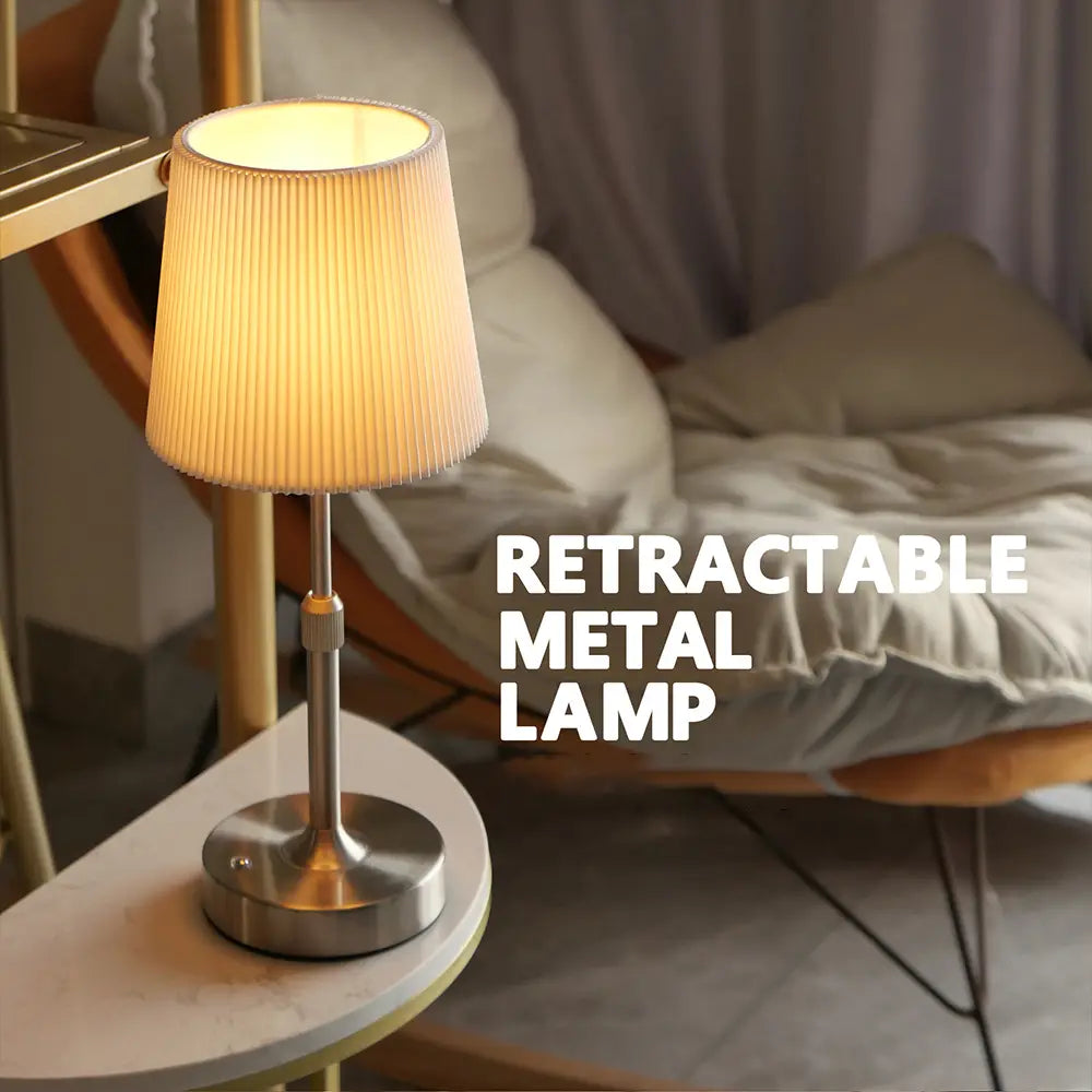 Ein warmtoniger, plissierter Lampenschirm auf einer eleganten metallischen Basis ist von vorn als Touch-Tischlampe auf einem kleinen Tisch dargestellt.