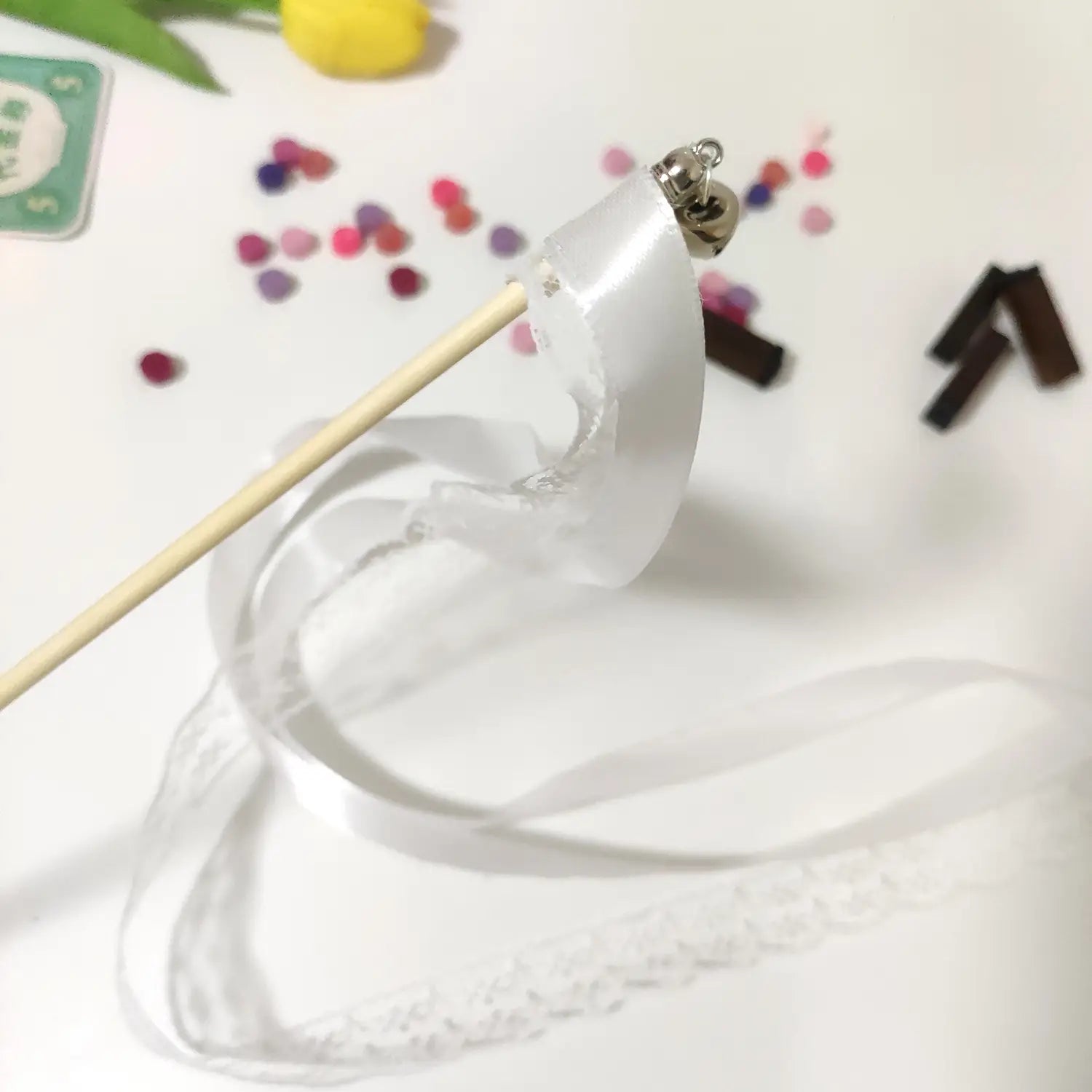 Baguettes de ruban de mariage avec de délicats rubans en satin blanc présentant un léger éclat et de petites breloques en forme de cloche en argent fixées en partie supérieure.