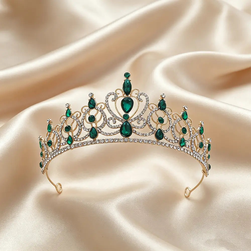 Un accessoire de coiffure de mariée en couronne de diadème baroque en strass doré, présentant une base ton sur ton doré, rehaussée de cristaux émeraude en forme de goutte et de strass transparents, dans un design ornemental évoquant une couronne.