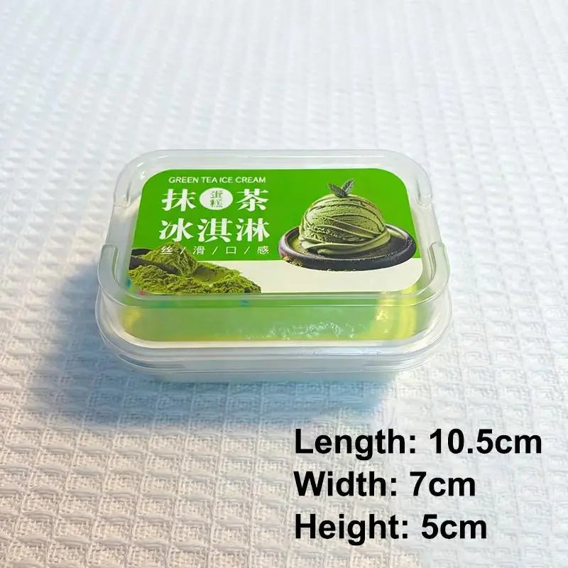 un recipiente de plástico transparente que contiene un vibrante pastel simulado de helado de matcha de color verde con caracteres chinos e una imagen del postre, diseñado como un juguete sensorial tipo fidget de crecimiento lento.