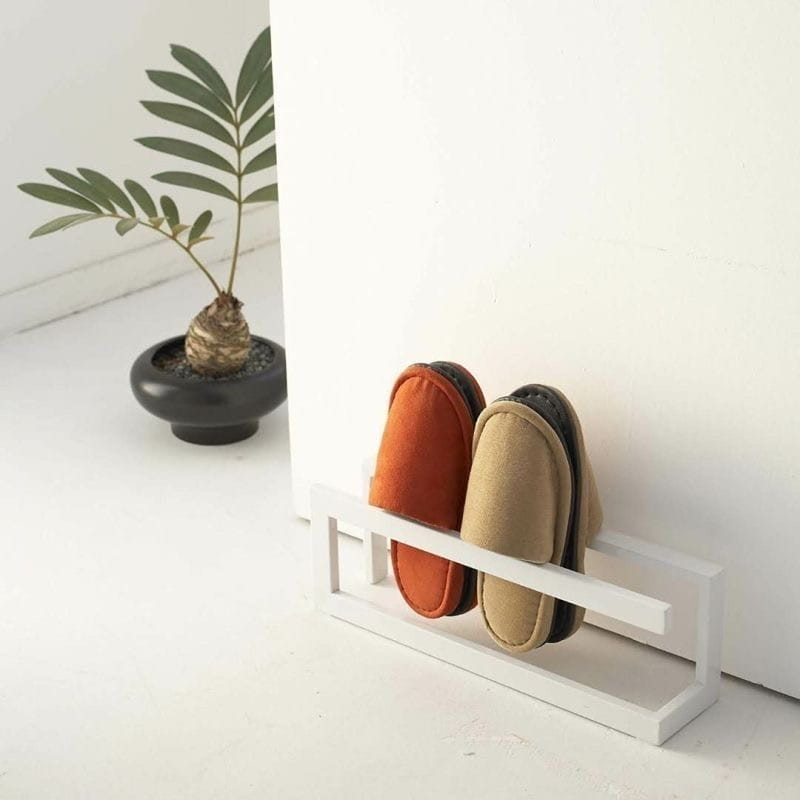 Weißes minimalistisches freistehendes Metall-Schuhregal mit einem Paar orangefarbener und beigerfarbener Schlupf-Slipper für platzsparende Lagerung.