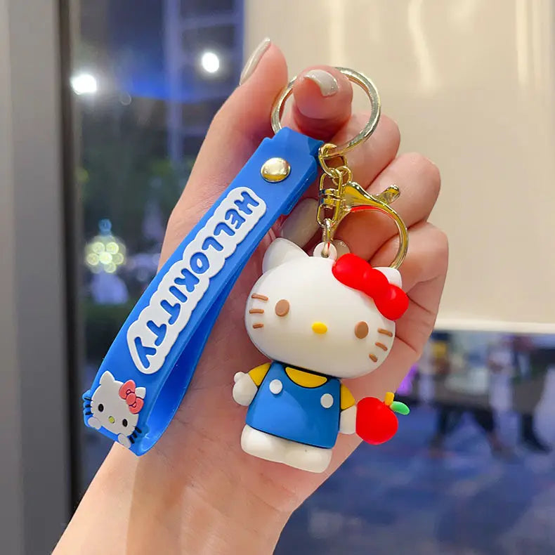 a white hello kitty cartoon keychain with a red bow and blue overalls holding a red apple attached to a blue wrist strap reading hello kitty for anime bag charm use