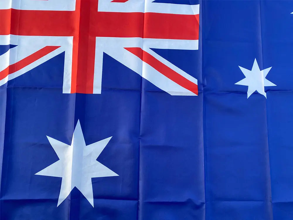 Bandera nacional australiana azul de 90x150 cm con un aspa de la bandera británica roja y blanca en la esquina superior izquierda y dos estrellas blancas grandes sobre un campo azul intenso.