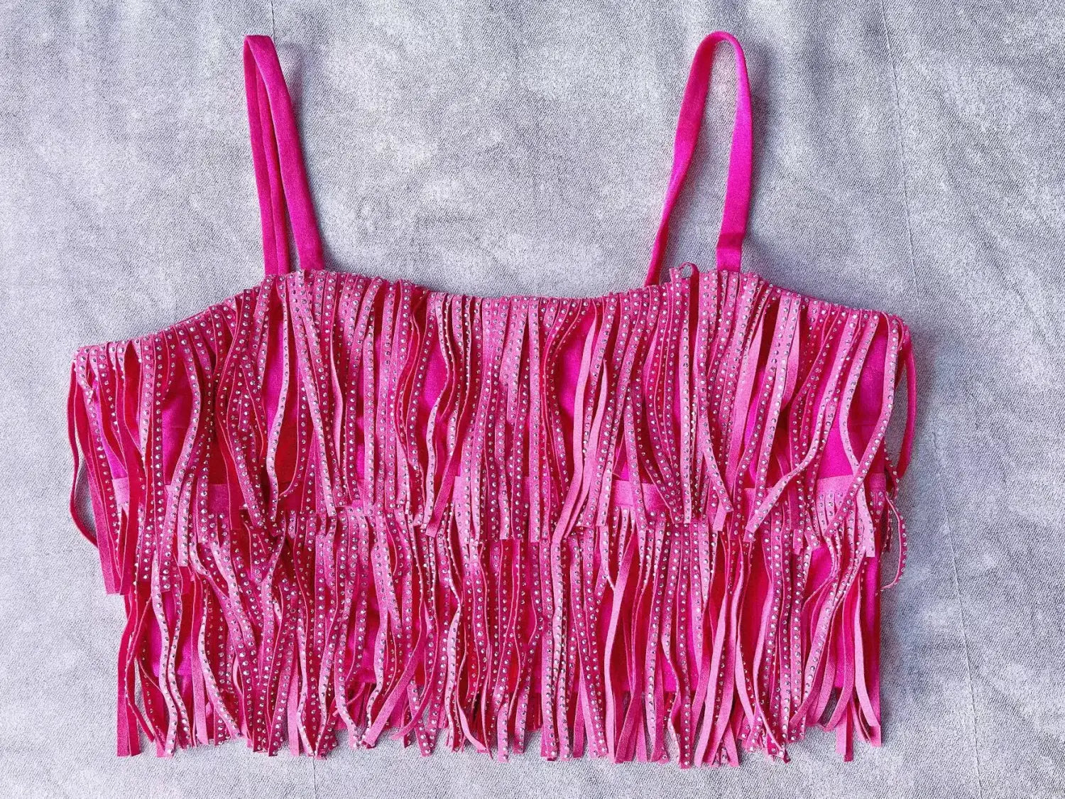 Haut court fuchsia vif à franges, avec fines bretelles et des détails en strass scintillants le long des franges, assorti à une mini-jupe taille haute à franges en strass.