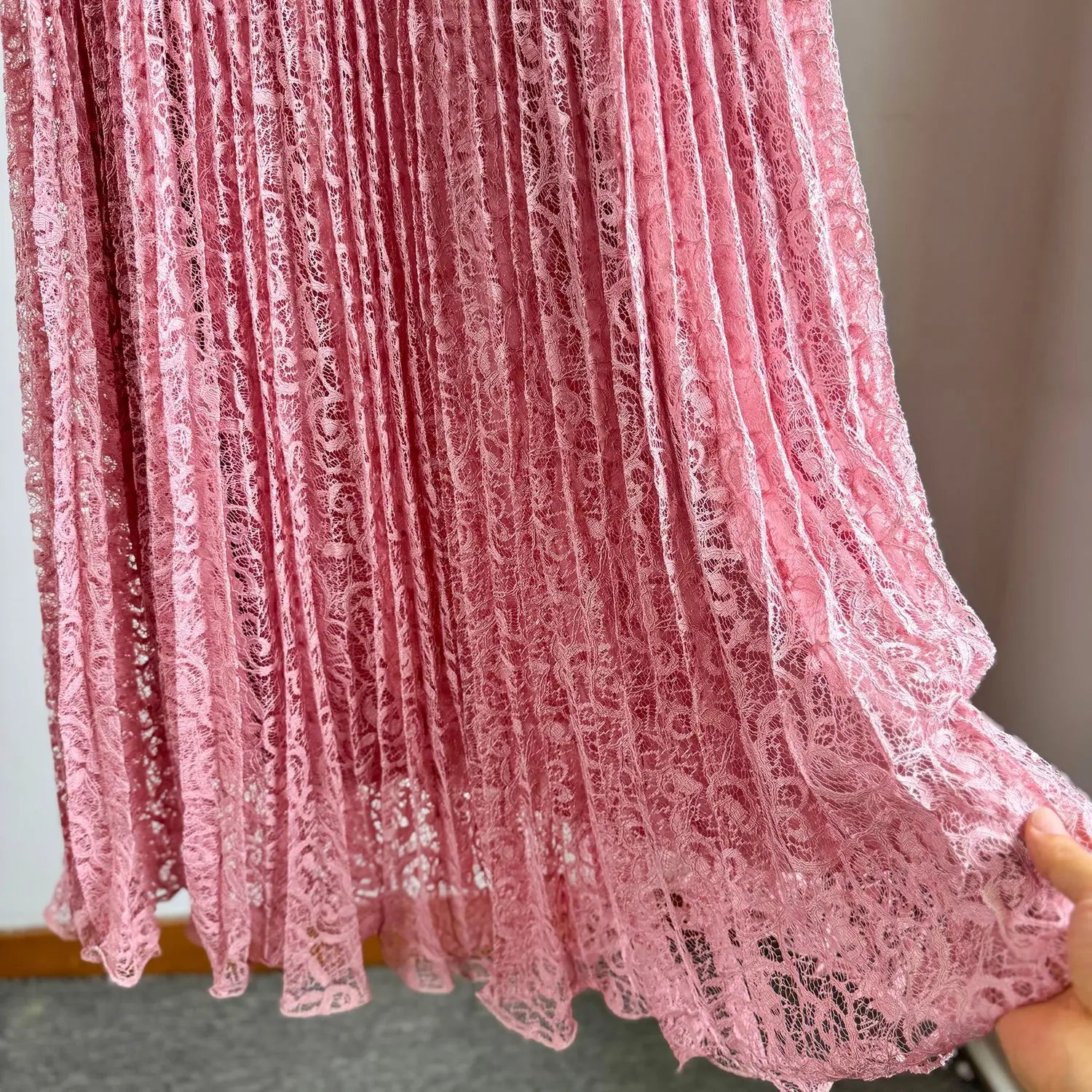 A delicate pink high waist pleated midi skirt made of semi-transparent lace fabric with intricate floral patterns suitable for Y2k streetwear.