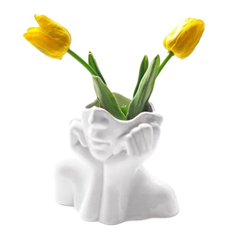 White ceramic abstract face makeup brush holder and vase shaped like a sculpted human head with hands cupping the face.