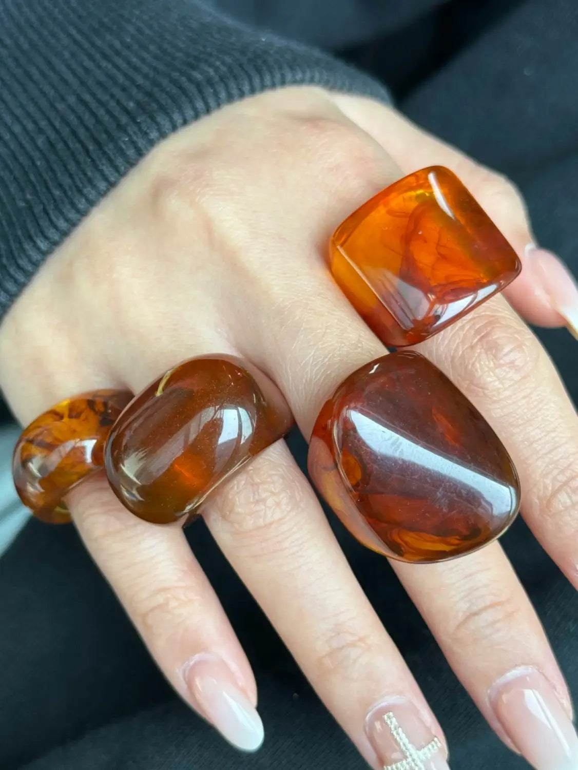 Set of three chunky amber-colored polished resin cocktail rings with a smooth glossy finish and natural marbled patterns.
