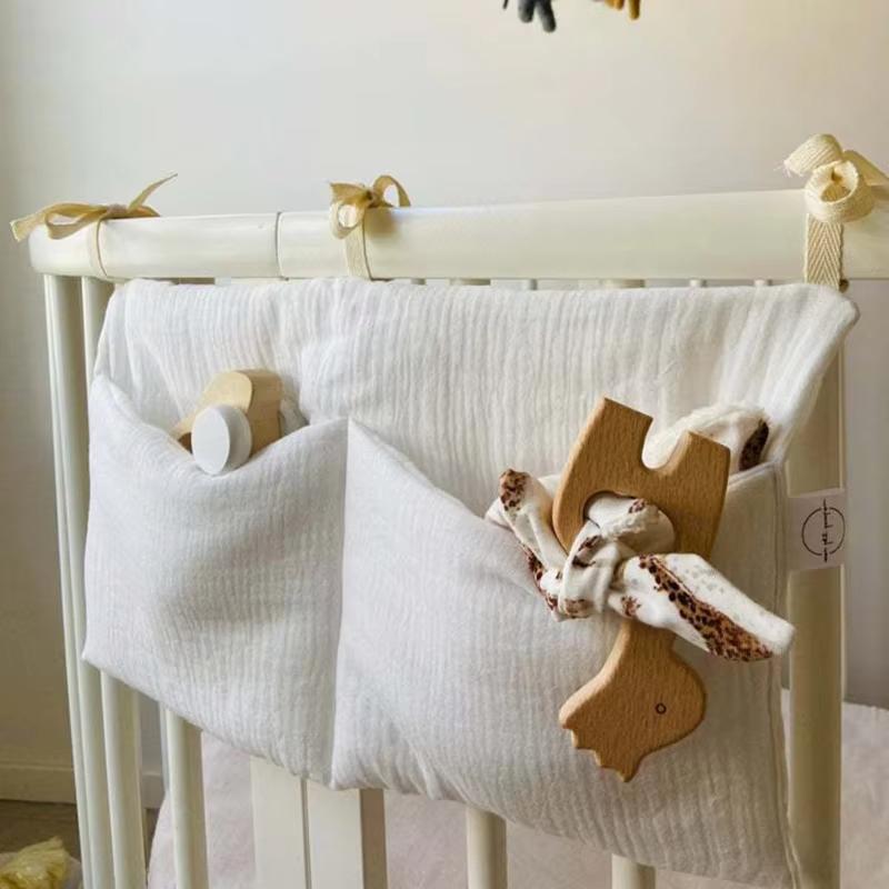 Weiße Baumwoll-Musselin-Wickeltisch-Einsatz-Aufbewahrungstasche für die Windelorganisation mit zwei Taschen, die Holzspielzeug und ein gemustertes Tuch aufnehmen.