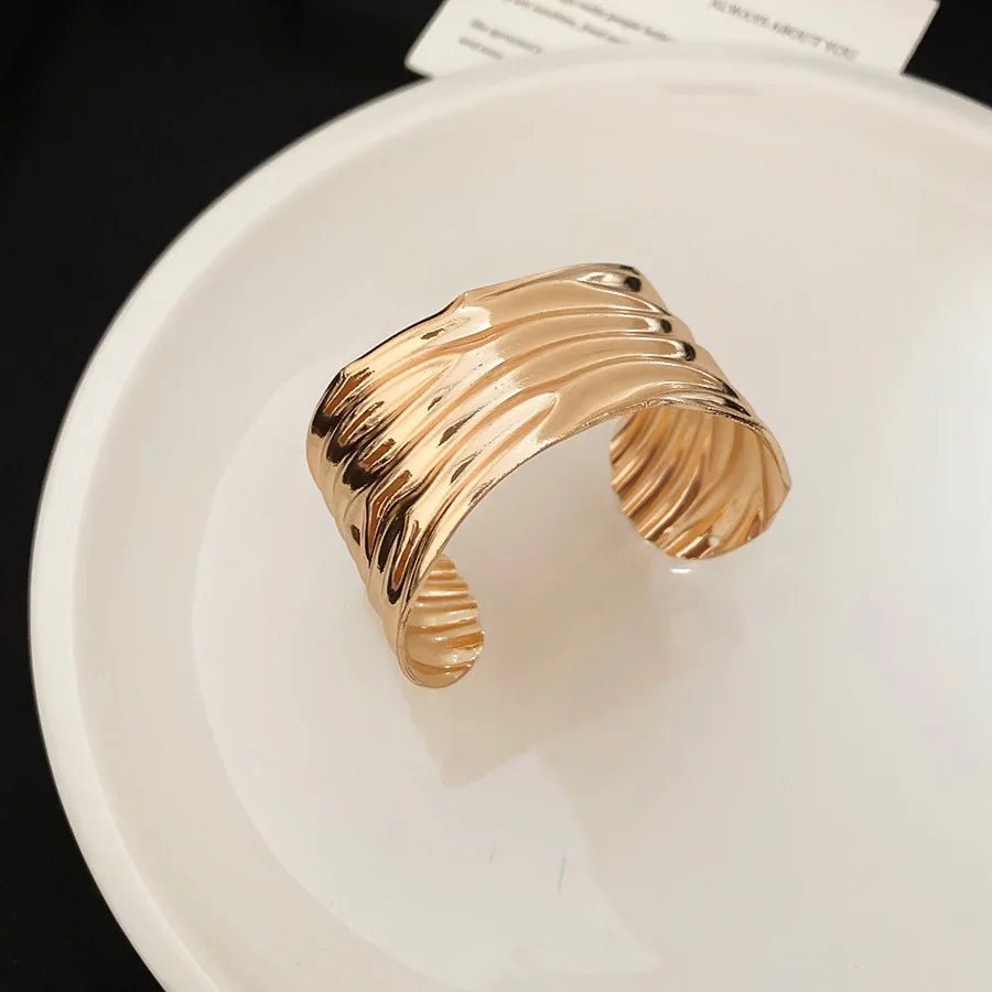 Gold-toned metallic pleated cuff bracelet for women with a textured wavy layered design.