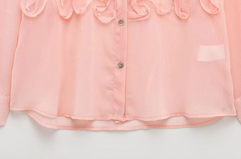 A delicate pink textured ruffled button up blouse with a pleated design and silver buttons down the front.