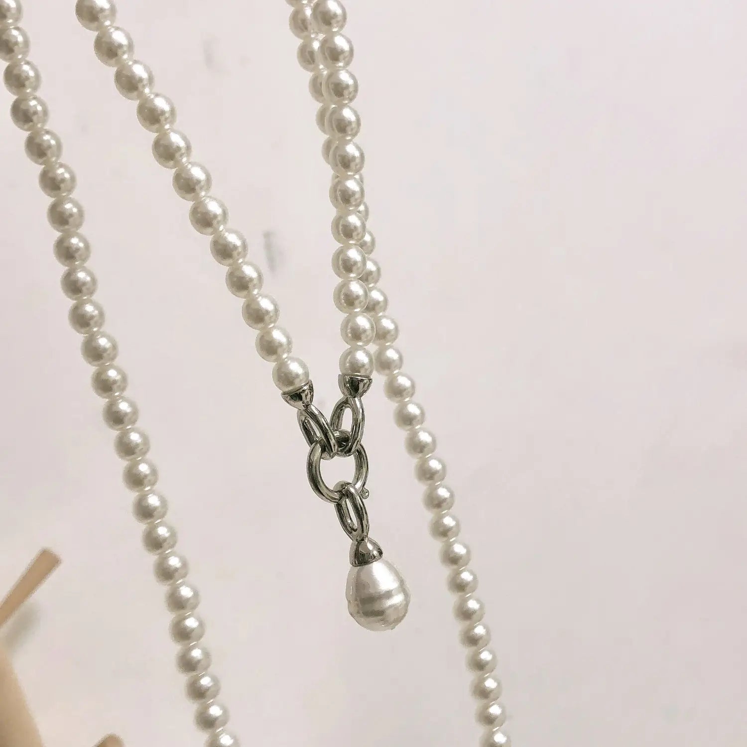 Un long collier en perles en pendentif pour femmes, composé d’un rang délicat de perles blanches uniformes avec une fermeture à l’aspect argenté et d’un pendentif assorti en forme de goutte de perle, assorti au long collier en pendentif de perles pour femmes.