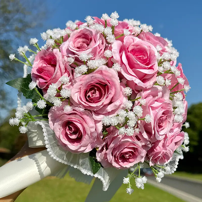 A delicate white silk rose wedding bouquet with pink roses and white babys breath accented with pearls and tied with a sheer lace ribbon.